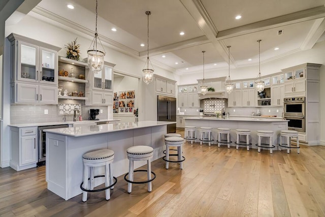 kitchen featuring a breakfast bar, decorative light fixtures, beverage cooler, a large island with sink, and light hardwood / wood-style floors