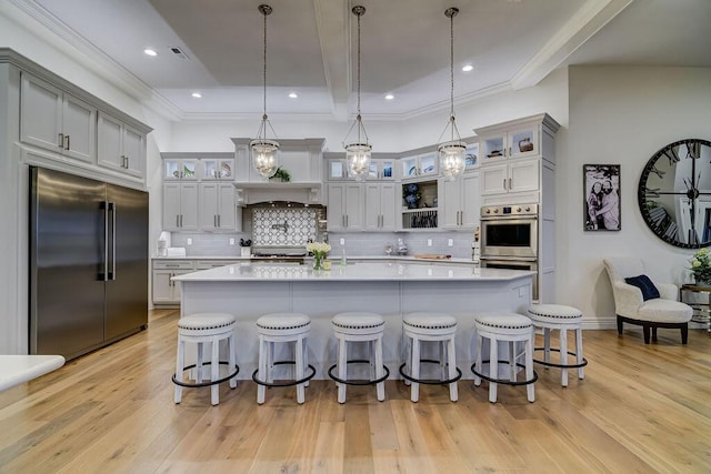 kitchen with appliances with stainless steel finishes, a kitchen bar, pendant lighting, and light hardwood / wood-style floors