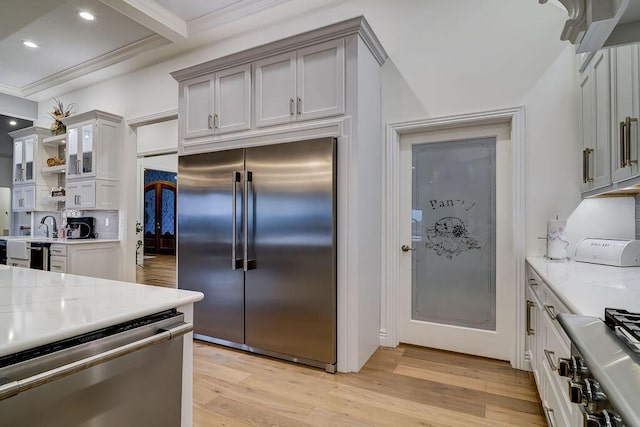 kitchen with crown molding, appliances with stainless steel finishes, light stone counters, light hardwood / wood-style floors, and decorative backsplash