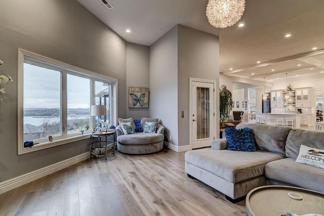 living room with a towering ceiling, a notable chandelier, and light hardwood / wood-style flooring