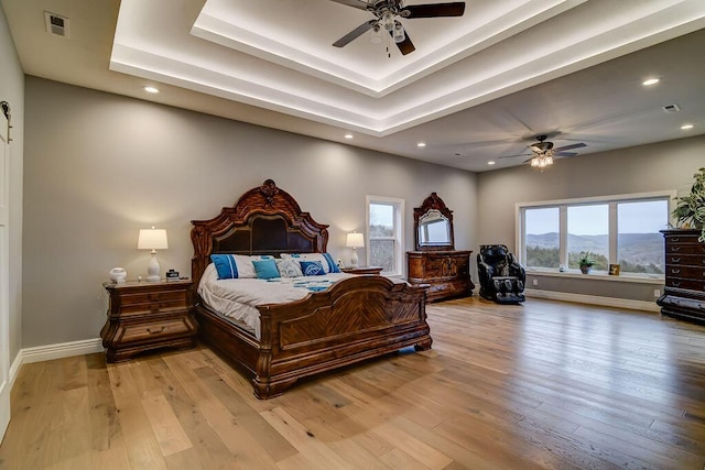 bedroom featuring light hardwood / wood-style flooring, a raised ceiling, and ceiling fan