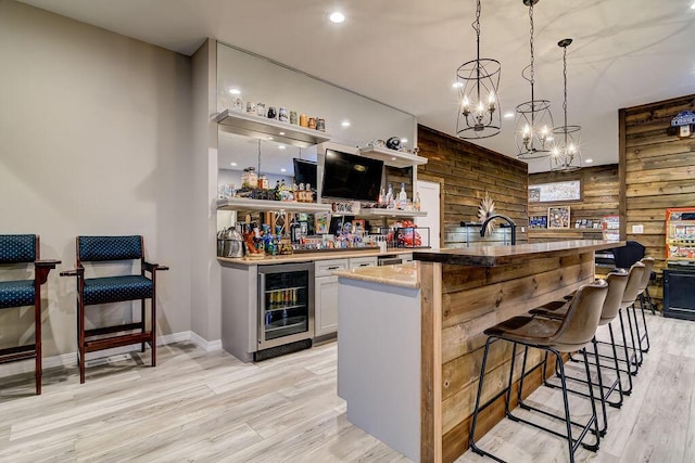 bar featuring pendant lighting, light hardwood / wood-style flooring, white cabinets, beverage cooler, and wood walls