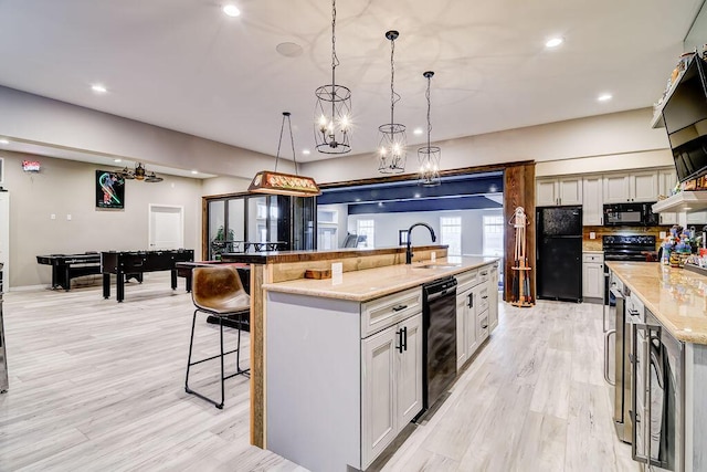 kitchen with a large island, sink, light stone counters, black appliances, and decorative light fixtures