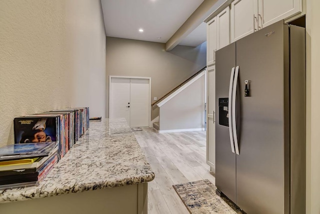 kitchen with stainless steel refrigerator with ice dispenser, white cabinetry, light stone counters, and light wood-type flooring