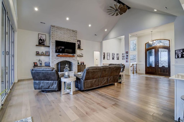 living room featuring a fireplace, high vaulted ceiling, french doors, and light wood-type flooring