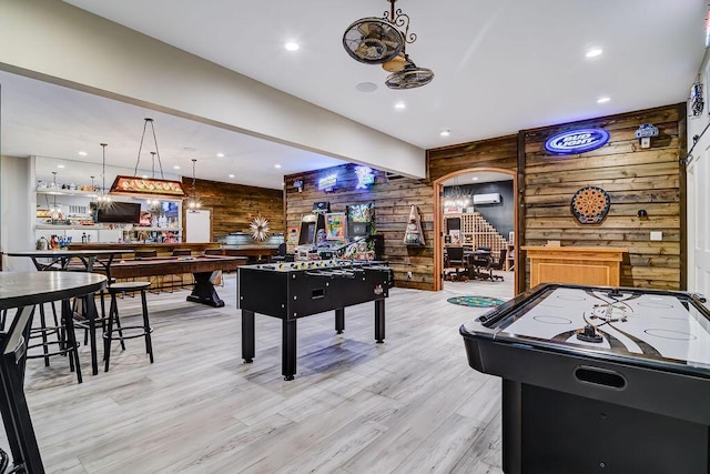 rec room featuring light hardwood / wood-style flooring, wooden walls, a wall mounted AC, and bar area