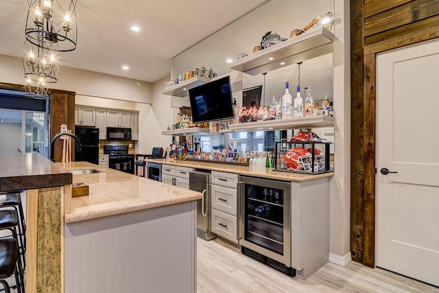 kitchen featuring beverage cooler, hanging light fixtures, stove, light hardwood / wood-style floors, and light stone countertops