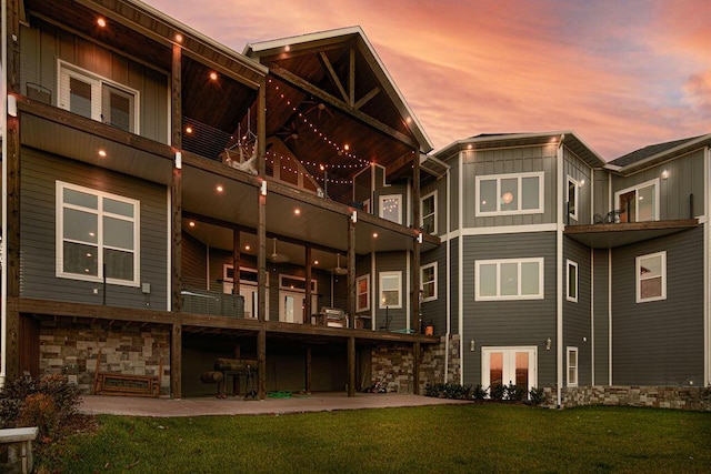 back house at dusk featuring a patio and a lawn