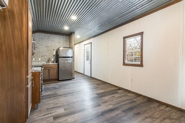 kitchen with brick wall, dark wood-type flooring, sink, and stainless steel fridge