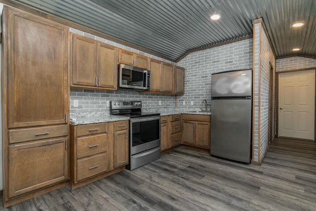 kitchen featuring stainless steel appliances, vaulted ceiling, brick wall, and dark hardwood / wood-style flooring