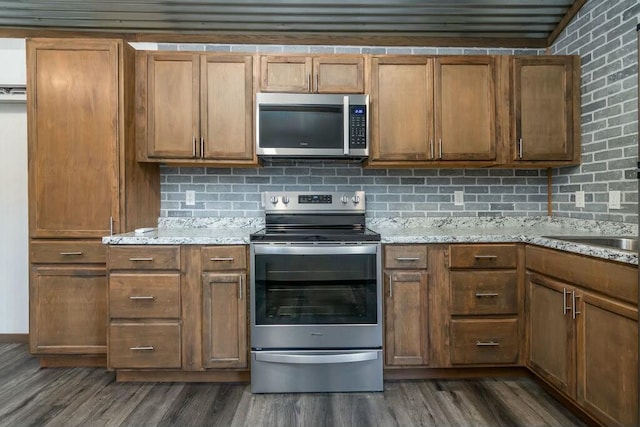 kitchen featuring light stone counters, appliances with stainless steel finishes, dark hardwood / wood-style flooring, and backsplash