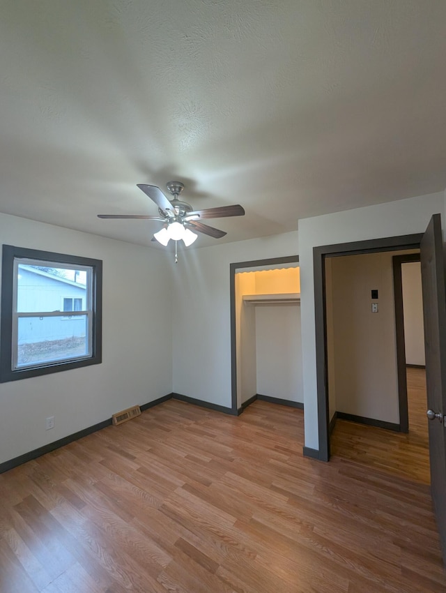 unfurnished bedroom with ceiling fan, light hardwood / wood-style flooring, and multiple closets