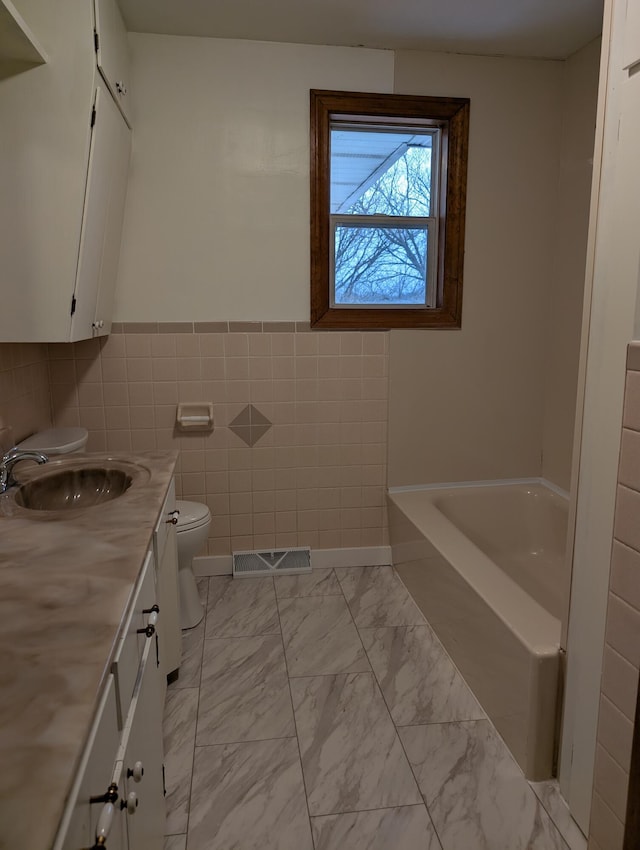 bathroom with vanity, a washtub, tile walls, and toilet