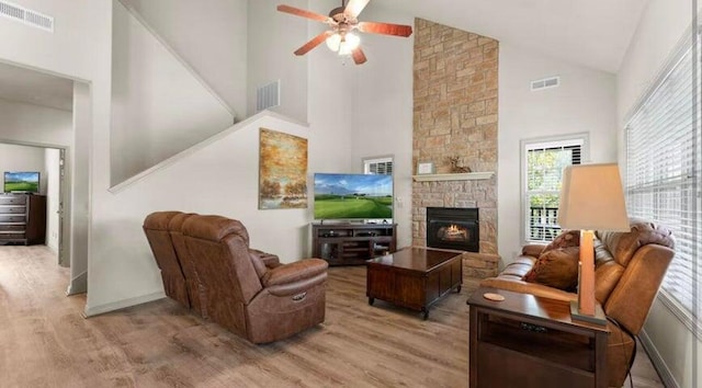 living room with hardwood / wood-style floors, a stone fireplace, high vaulted ceiling, and ceiling fan