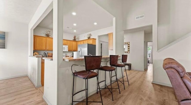 kitchen featuring a kitchen breakfast bar, light hardwood / wood-style floors, stainless steel fridge with ice dispenser, and kitchen peninsula