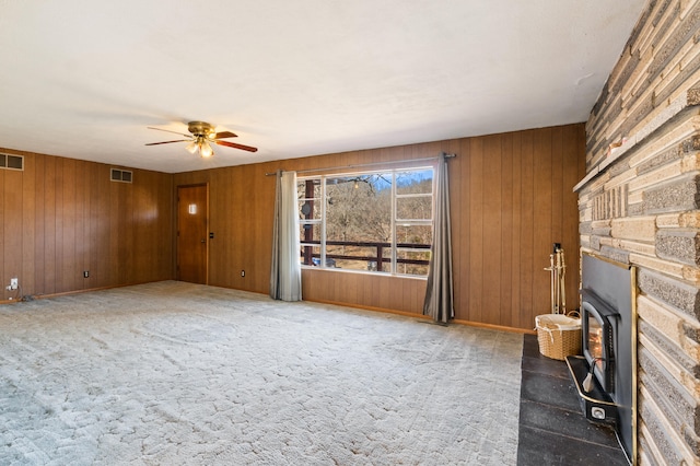 unfurnished living room featuring a fireplace, wood walls, ceiling fan, and carpet