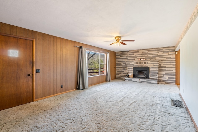 unfurnished living room featuring a stone fireplace, wood walls, ceiling fan, and carpet flooring