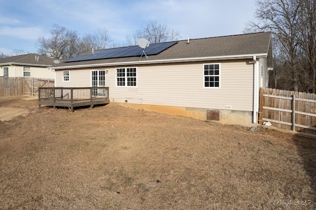 rear view of property featuring a wooden deck and solar panels