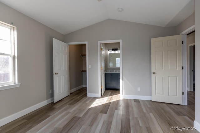 unfurnished bedroom with vaulted ceiling, a spacious closet, light hardwood / wood-style floors, and a closet