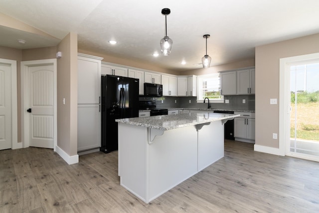 kitchen with sink, a center island, light stone counters, black appliances, and decorative backsplash