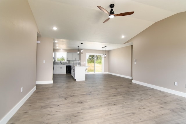 unfurnished living room featuring hardwood / wood-style flooring, sink, ceiling fan with notable chandelier, and vaulted ceiling