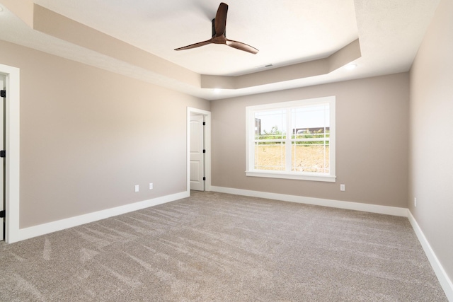 unfurnished room featuring a raised ceiling, carpet, and ceiling fan