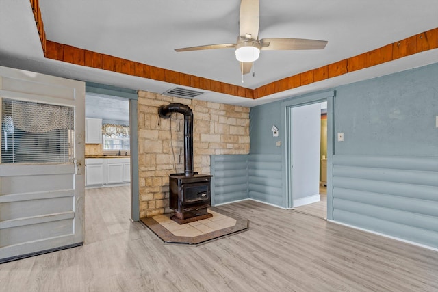 living room featuring ceiling fan, a raised ceiling, light hardwood / wood-style floors, and a wood stove