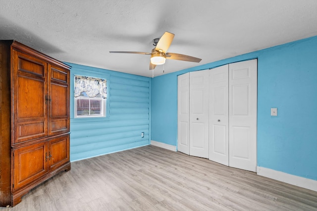 unfurnished bedroom with a textured ceiling, a closet, ceiling fan, log walls, and light hardwood / wood-style floors