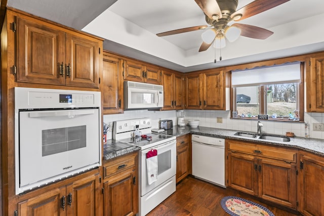 kitchen with dark wood-style floors, tasteful backsplash, brown cabinetry, a sink, and white appliances