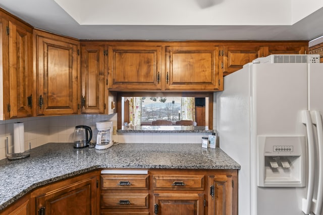 kitchen with stone counters, tasteful backsplash, white fridge with ice dispenser, and brown cabinets