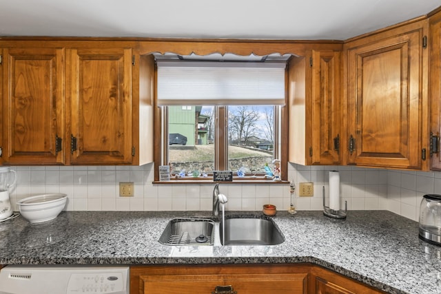 kitchen with dark stone counters, backsplash, a sink, and brown cabinets