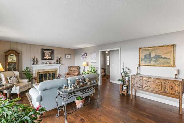 living area featuring a textured ceiling, dark wood-style flooring, a brick fireplace, and baseboards