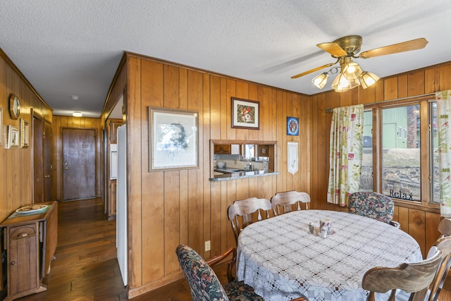 dining area with dark wood-type flooring, a textured ceiling, wooden walls, and a ceiling fan