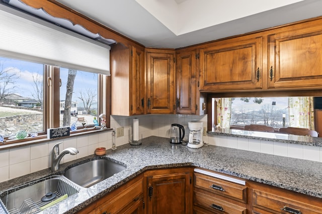 kitchen featuring decorative backsplash, dark stone countertops, a sink, and brown cabinets