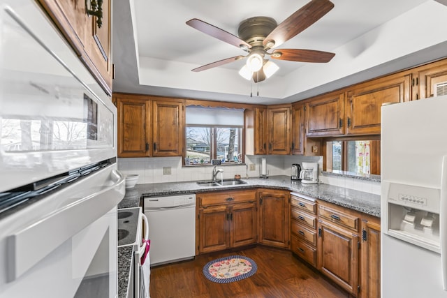 kitchen with sink, white appliances, dark hardwood / wood-style floors, a raised ceiling, and dark stone counters