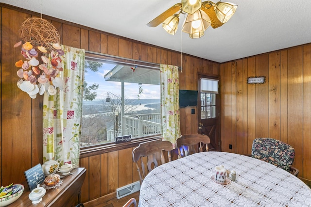 dining space featuring ceiling fan and wood walls