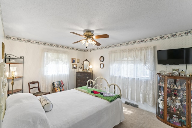 bedroom with a textured ceiling, ceiling fan, carpet floors, visible vents, and wallpapered walls