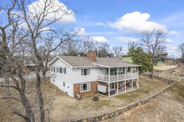 rear view of house with roof with shingles, brick siding, a chimney, and a patio area