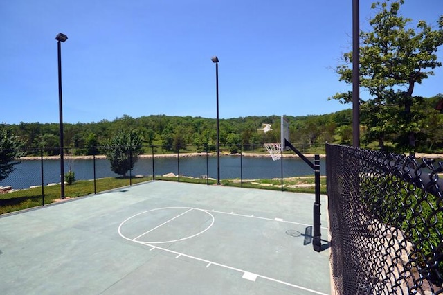 view of sport court featuring community basketball court, a water view, fence, and a view of trees