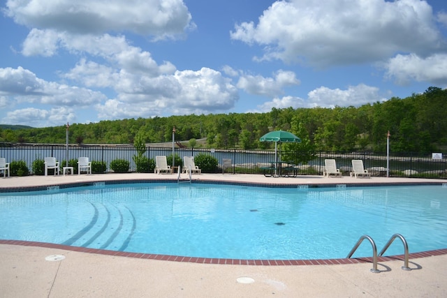 view of swimming pool with a patio area, fence, and a wooded view