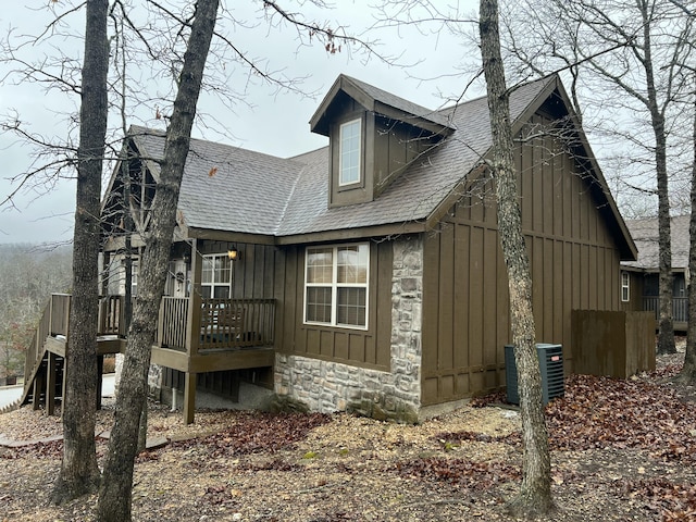 view of home's exterior featuring stone siding, roof with shingles, a deck, cooling unit, and board and batten siding