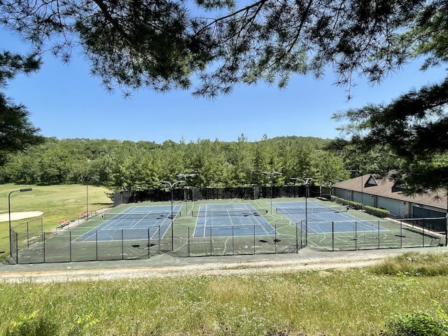 view of sport court with fence and a view of trees