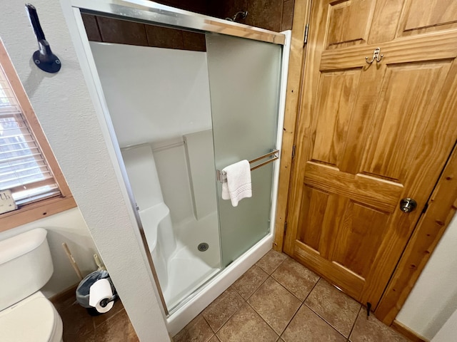 bathroom featuring tile patterned flooring, a shower stall, and toilet