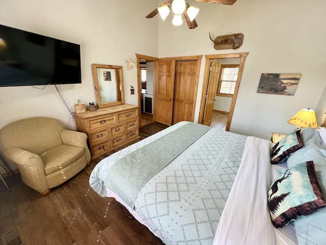 bedroom with visible vents, a towering ceiling, a ceiling fan, connected bathroom, and wood finished floors