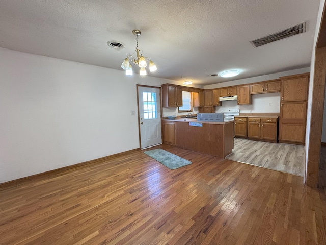 kitchen with hardwood / wood-style floors, a textured ceiling, decorative light fixtures, kitchen peninsula, and a chandelier