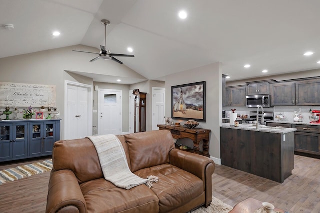 living room featuring sink, light hardwood / wood-style flooring, ceiling fan, and vaulted ceiling