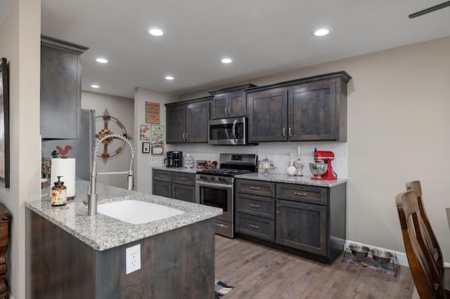 kitchen with light hardwood / wood-style flooring, dark brown cabinets, light stone countertops, and appliances with stainless steel finishes