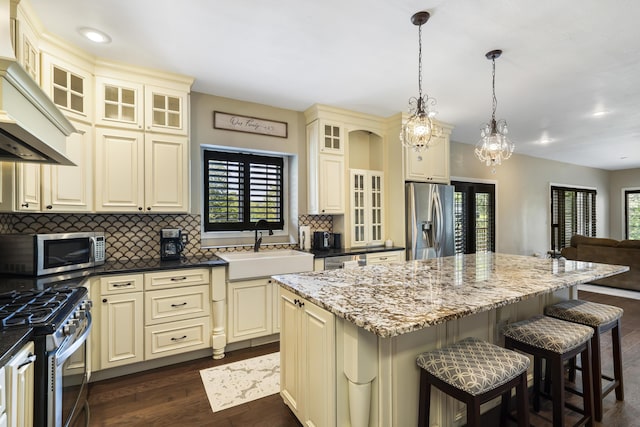 kitchen featuring sink, appliances with stainless steel finishes, a kitchen island, pendant lighting, and cream cabinets