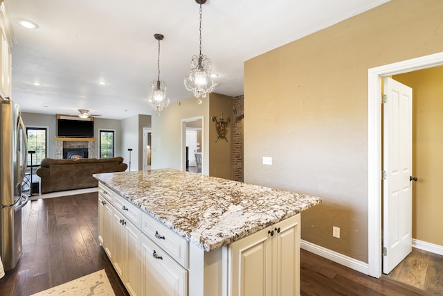 kitchen featuring pendant lighting, stainless steel fridge, white cabinetry, light stone countertops, and a kitchen island