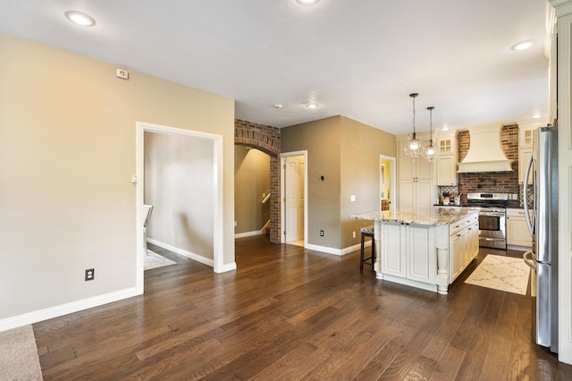 kitchen with custom exhaust hood, a center island, appliances with stainless steel finishes, a kitchen breakfast bar, and pendant lighting